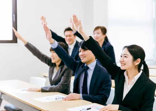 研修中の明るい会議室で手を挙げて積極的に参加している男女のビジネスパーソンのグループ。