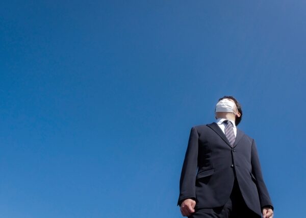 ビジネススーツを着た男性が目隠しをされて空を背に立つイメージ