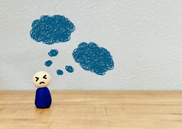 悩みの表情をしたフィギュアに上から降りかかる雨雲のイラストが描かれており、ストレスの感情的影響を象徴している